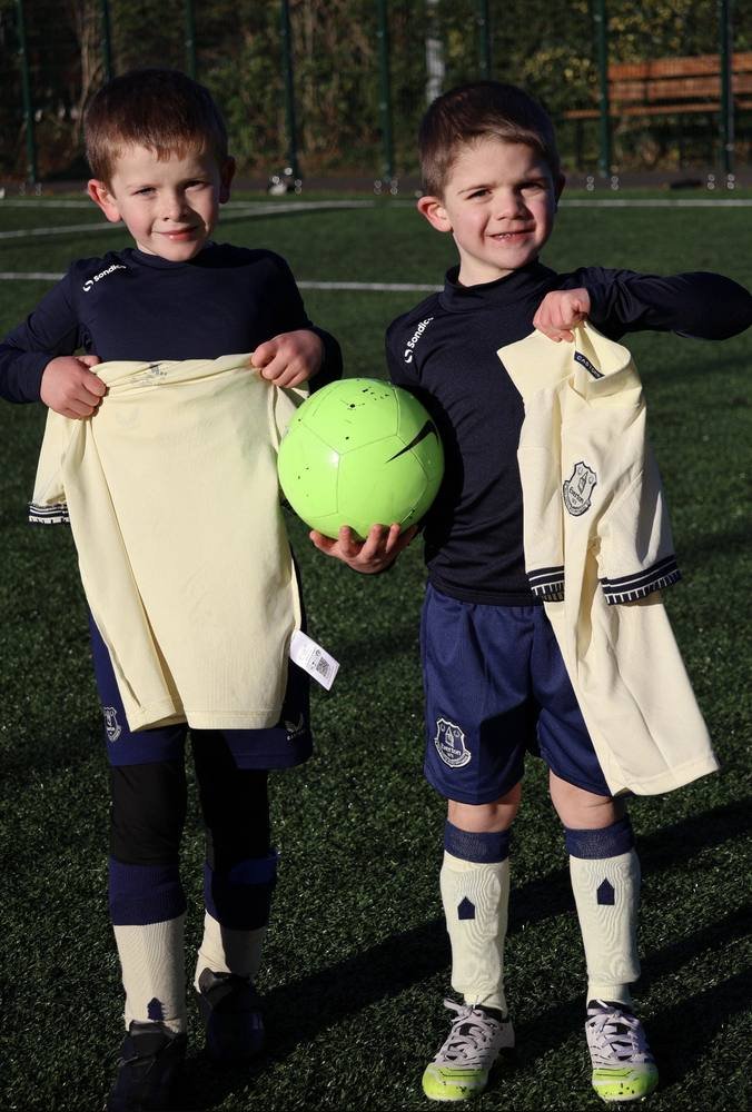 Two young players holding up their kit and a bright green football